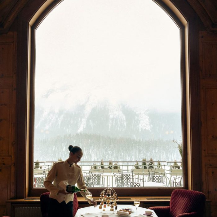 Guest at a tall window overlooking snowy mountains at Badrutt's Palace Hotel, St Moritz