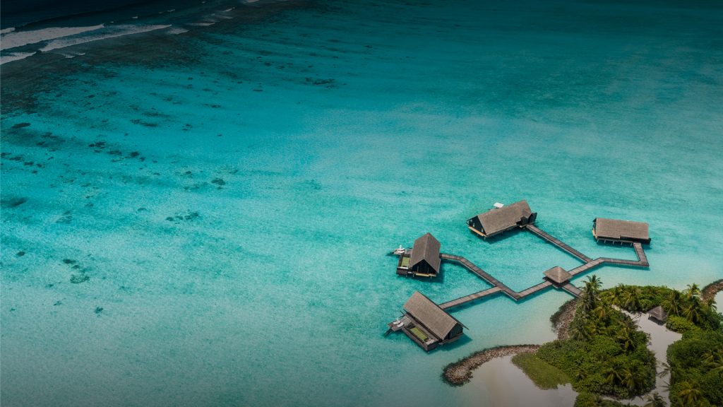 Overwater villas connected by walkways extend into turquoise lagoon waters at Reethi Rah, Maldives.