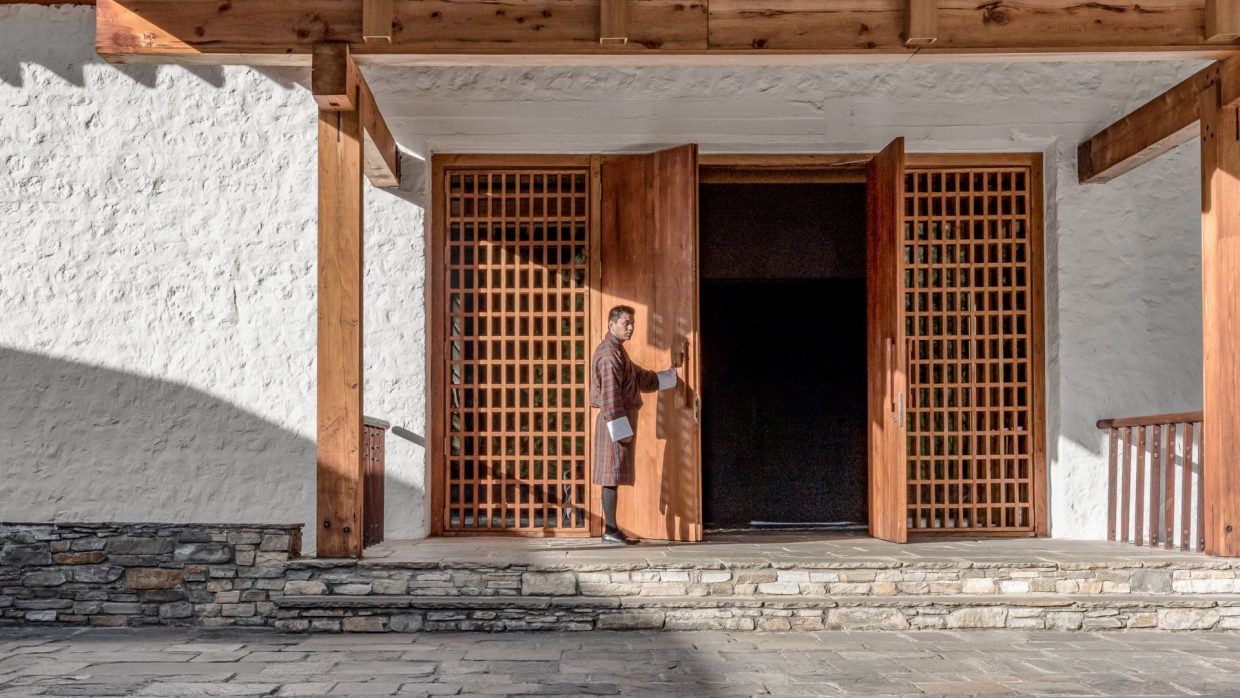 A man opening a door in traditional Bhutanese clothing