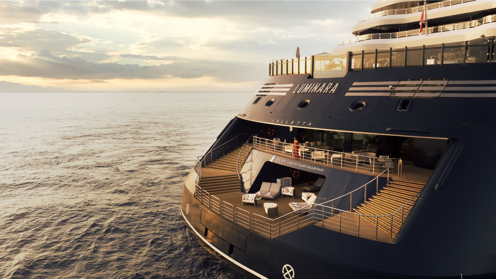 Aft view of Luminara by The Ritz-Carlton Yacht Collection at sea during golden hour, with terraces and lounge seating visible.