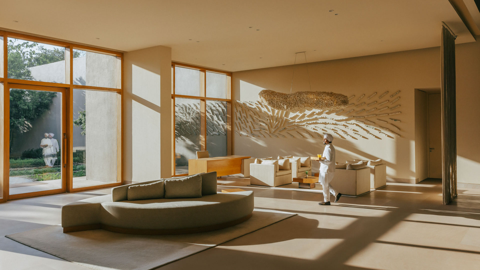 Sunlit minimalist lobby at Six Senses Vana with cream seating, large windows, and a staff member carrying refreshments.
