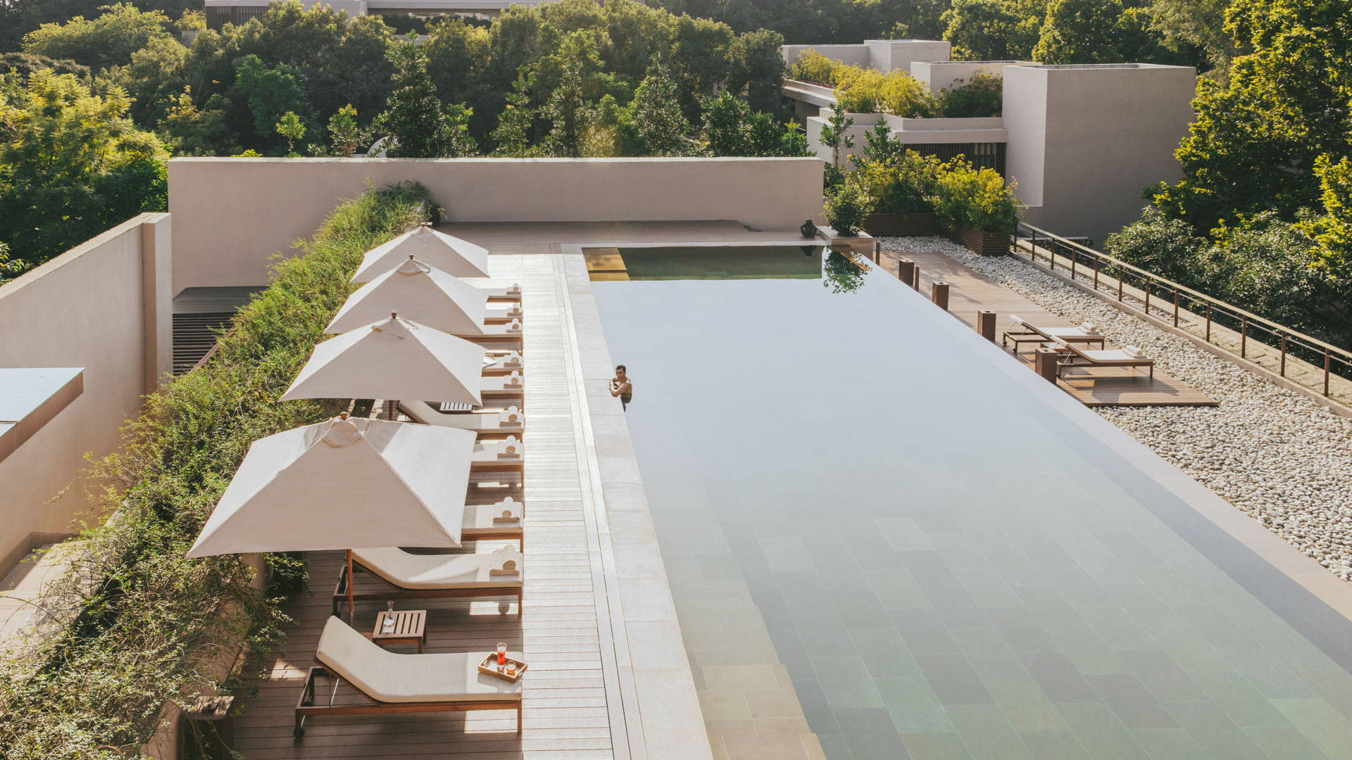 Long outdoor swimming pool at Six Senses Vana lined with white umbrellas, lounge chairs, and surrounding greenery.