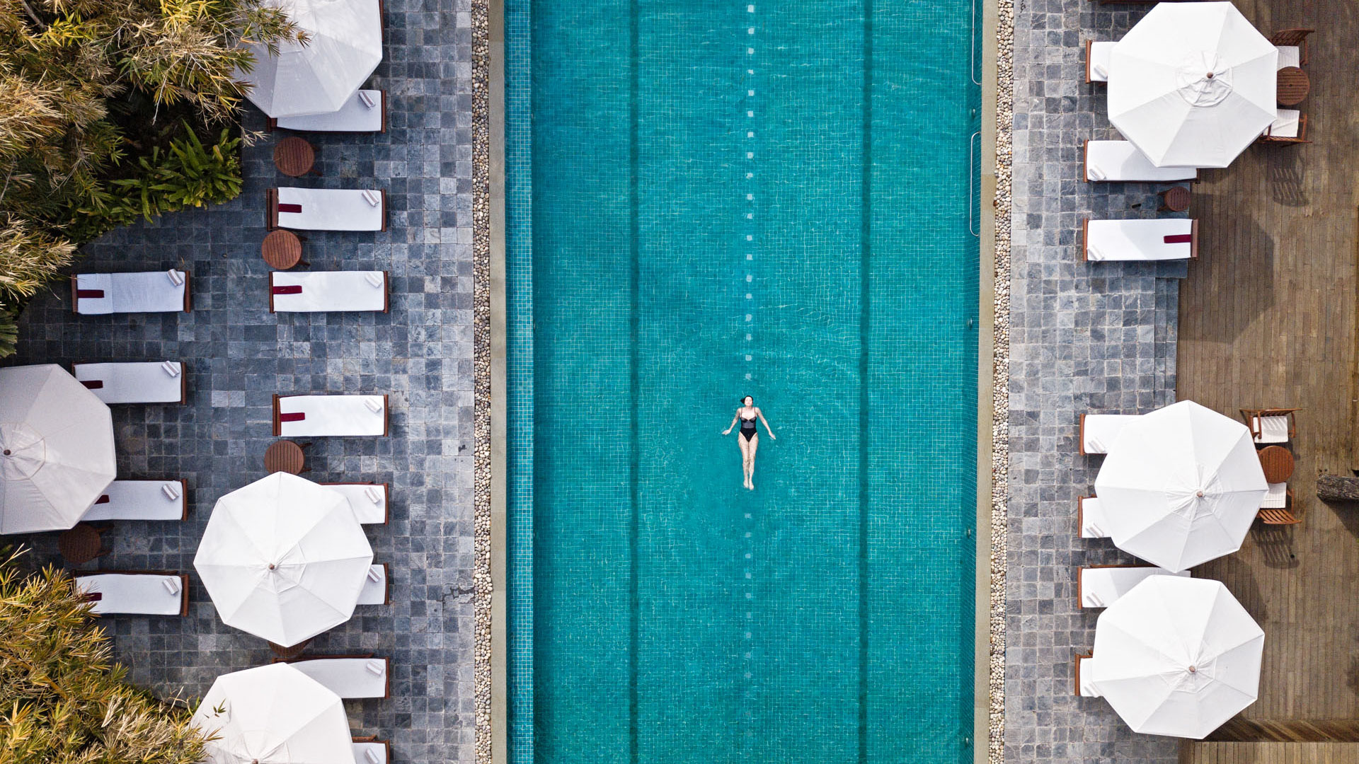 Aerial view of a guest floating in the outdoor pool at Ananda in the Himalayas, surrounded by loungers and white umbrellas.