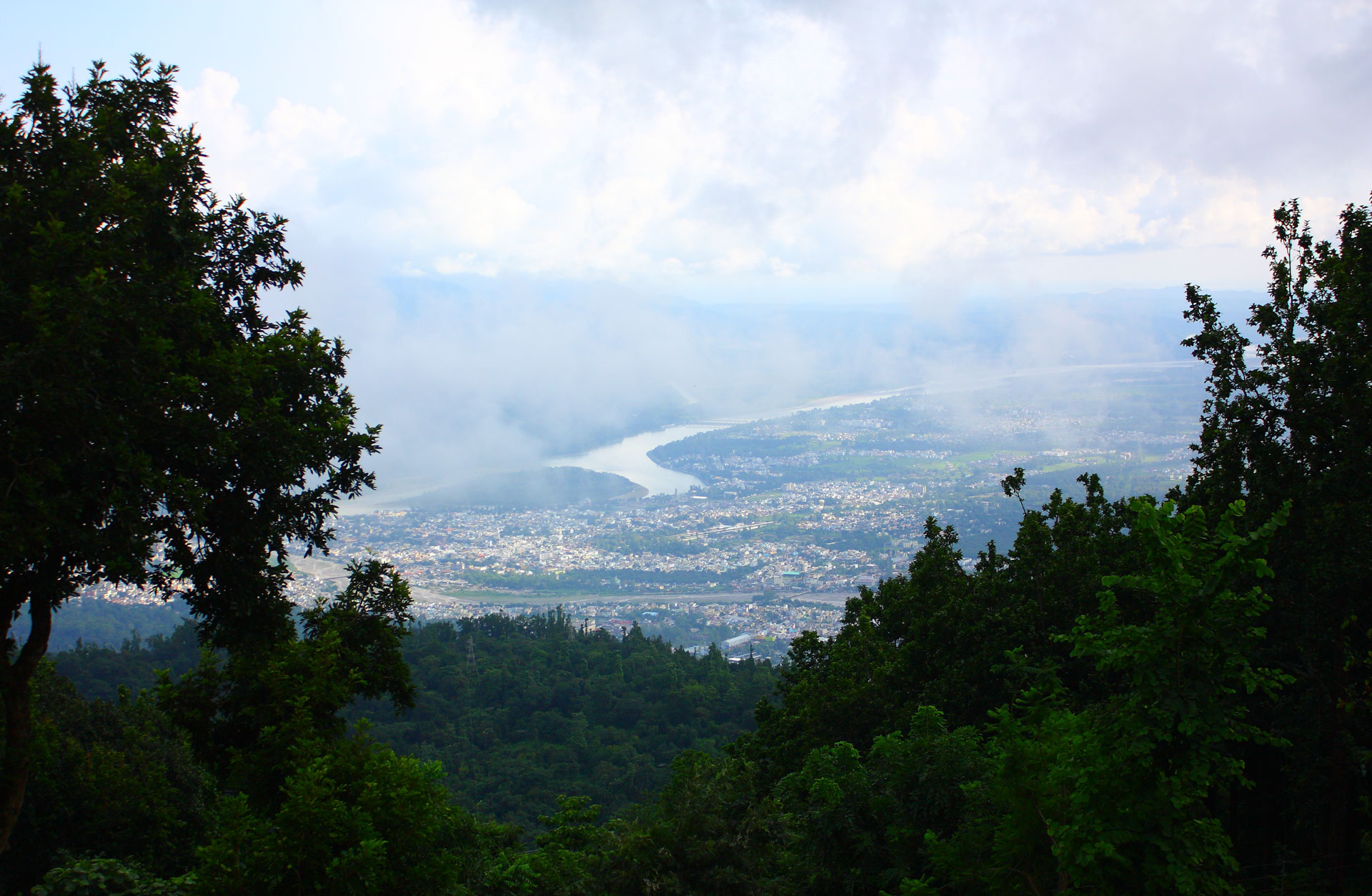 View from Ananda in the Himalayas overlooking forested hills, a winding river, and the valley below beneath dramatic clouds.