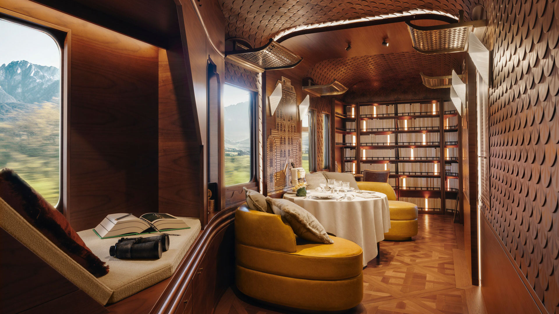 Luxurious suite interior aboard the Venice Simplon-Orient-Express, featuring warm wood paneling, curved seating, a dining table, and mountain views through large windows.