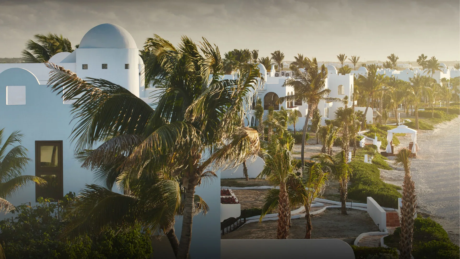 White domed beachfront villas and palm-lined paths at Belmond Cap Juluca in warm coastal light