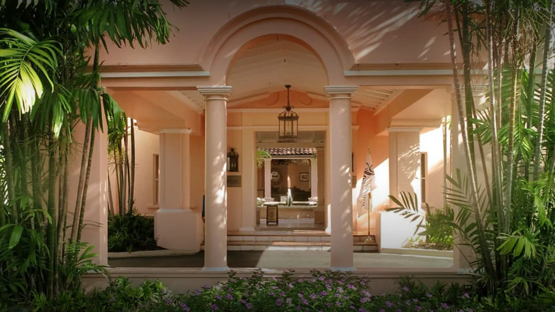 Entrance to Fairmont Royal Pavilion in Barbados framed by tropical plants, soft pink walls, and white columns.