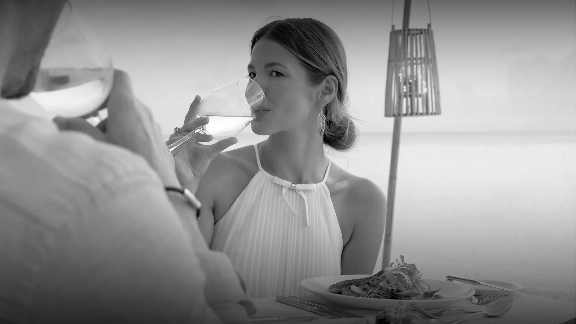 Couple dining by the beach at Fairmont Royal Pavilion in Barbados, raising glasses over an oceanfront dinner table