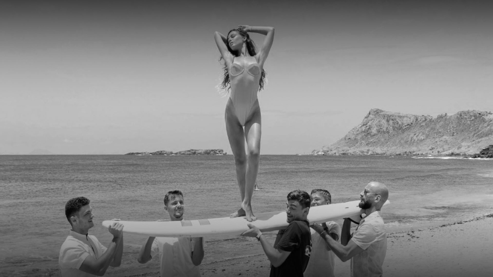 Black-and-white beach scene with woman standing on a surfboard held by four men at Hotel Le Toiny