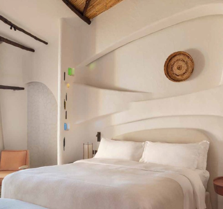 Sculpted white walls and woven wall basket above the bed in a room at Hotel Cala di Volpe
