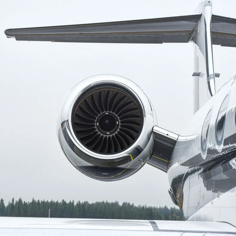 Close-up of a private jet's rear engine and polished chrome nacelle, with the tail wing above against an overcast sky.