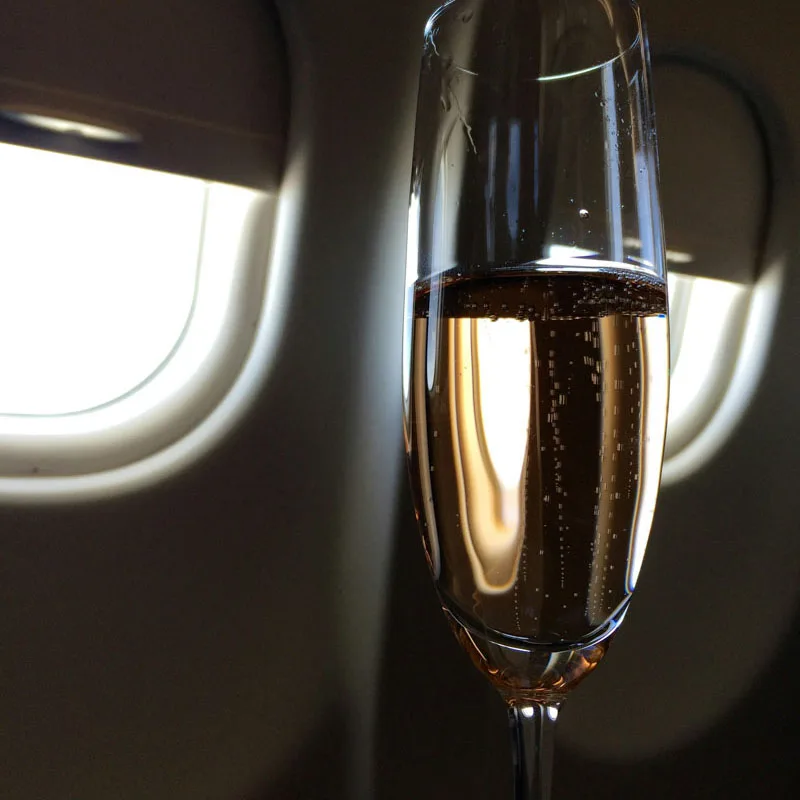 A glass of champagne catching soft daylight beside an aircraft cabin window