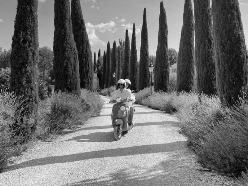 Couple riding a Vespa down the lavender-lined drive at Borgo Santo Pietro