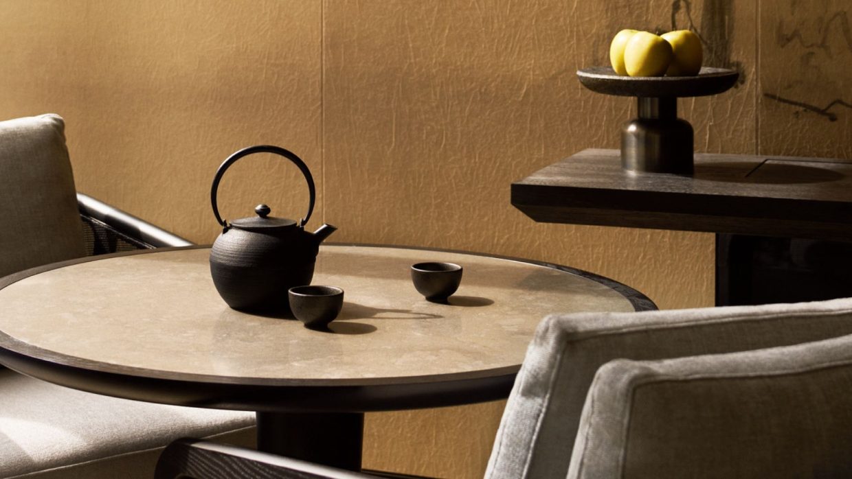 A cast iron teapot and two cups on a round stone table against a gold wall