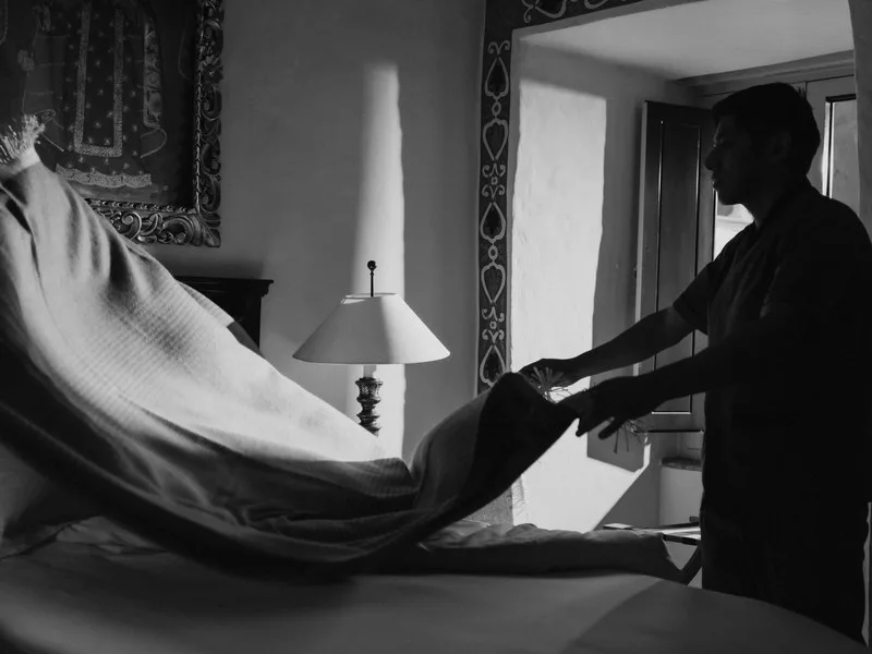 A silhouetted figure turning down a bed at dusk, in black and white