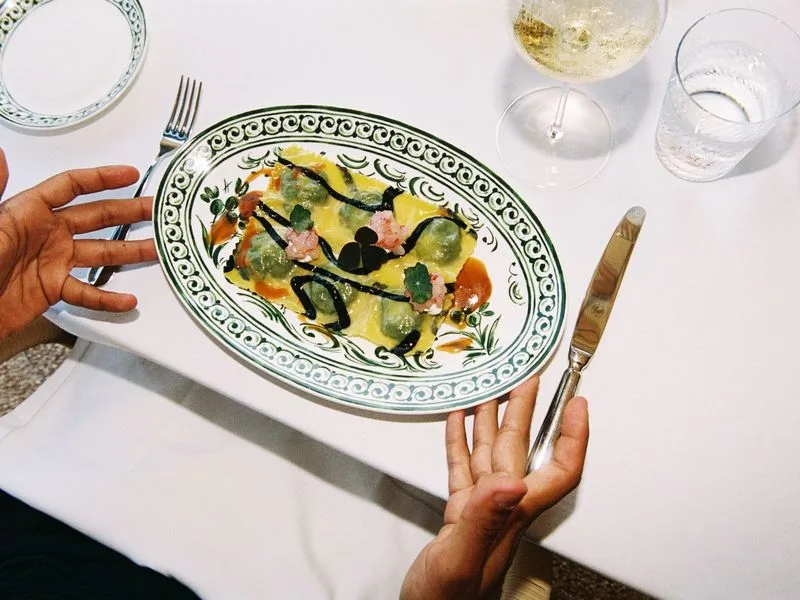 Hands presenting a plated dish on hand-painted green and white ceramic, wine glass alongside