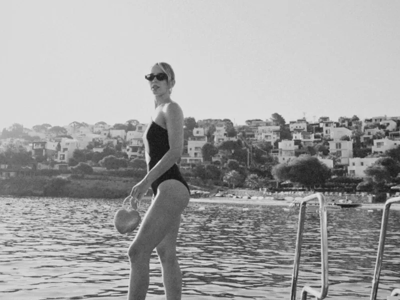 A woman in a black swimsuit on the jetty with the white houses of Yalıkavak behind, in black and white