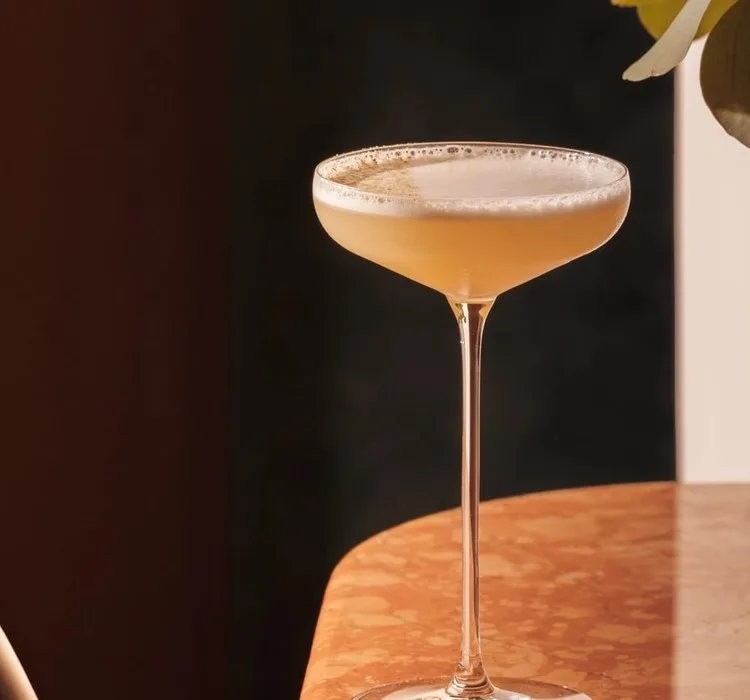 A coupe cocktail catching the light on a russet marble table at Jumeirah Marsa Al Arab