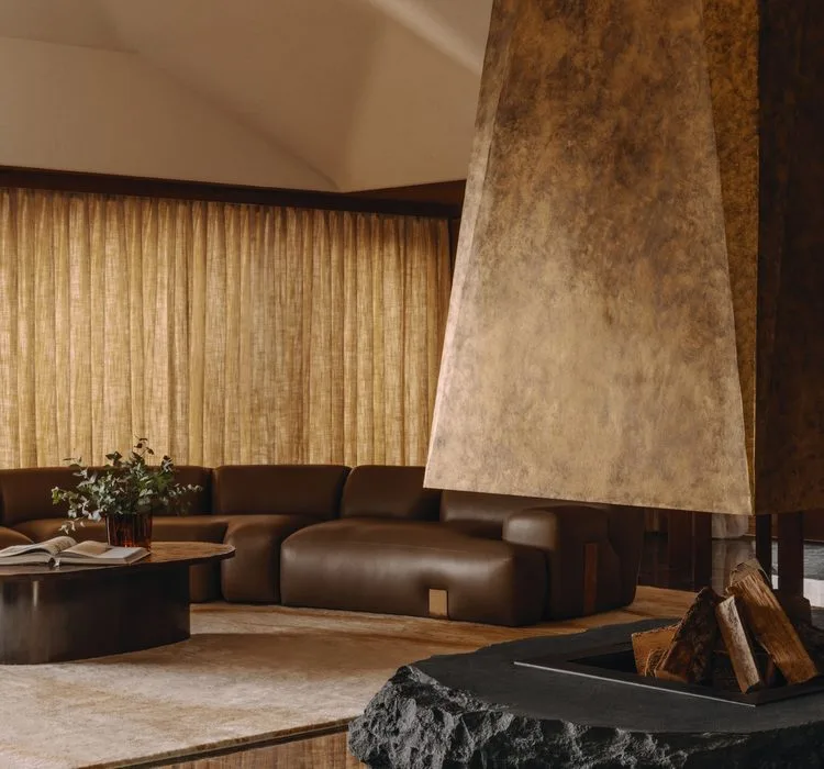 A sculptural copper-clad fireplace beside sheepskin armchairs