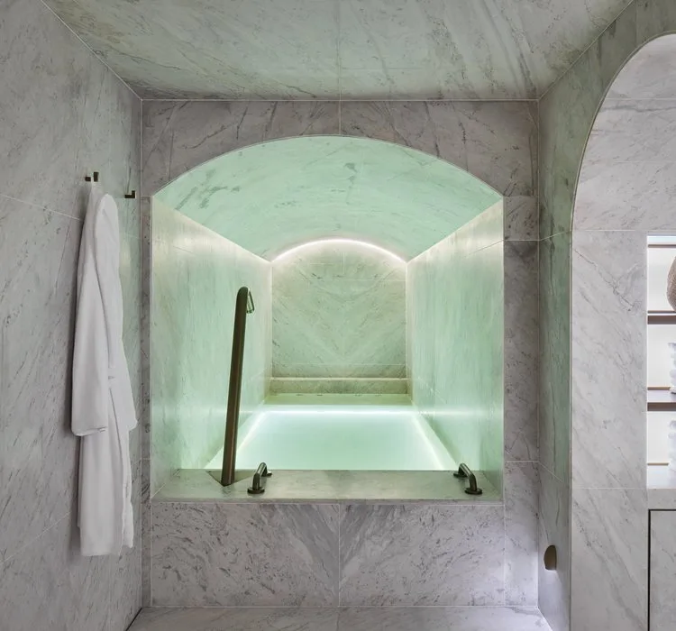 Marble hydrotherapy plunge pool glowing pale green beneath an arched ceiling at the Asaya Spa