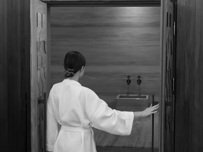 A woman in a robe opening the carved timber doors to the spa