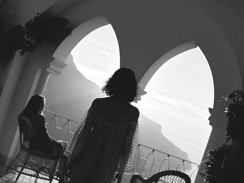 Two guests silhouetted in Gothic arched windows above the sea, in black and white, at Caruso, A Belmond Hotel