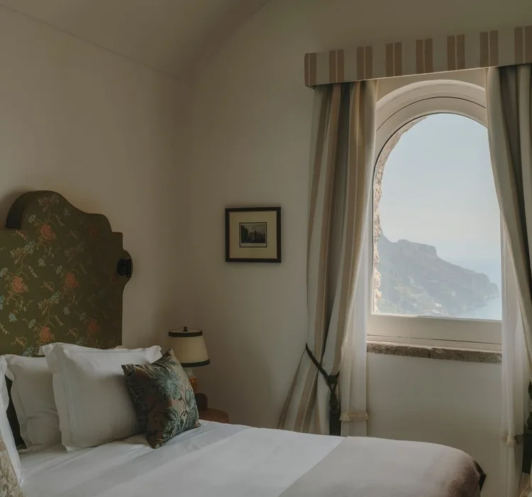 Calm guest room with a carved headboard and an arched window looking out to the coast