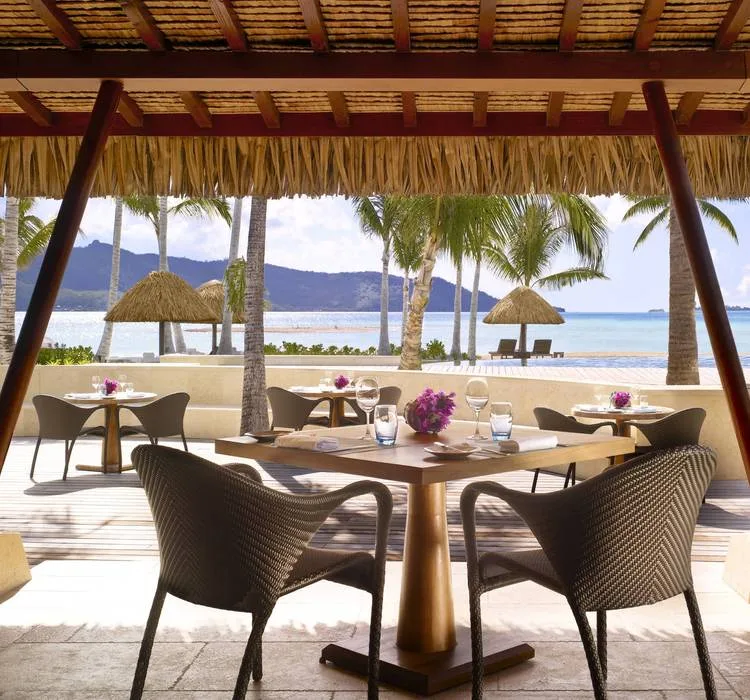 Beachside restaurant tables under a thatched roof facing the lagoon at Four Seasons Resort Bora Bora