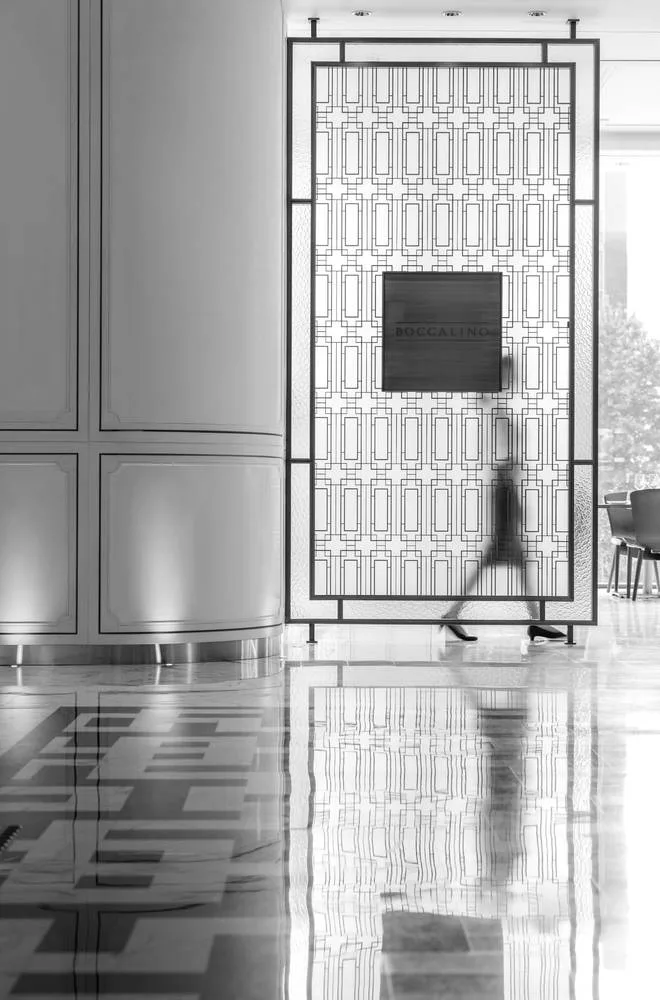A figure passing a tall latticed screen across the marble lobby floor, in black and white