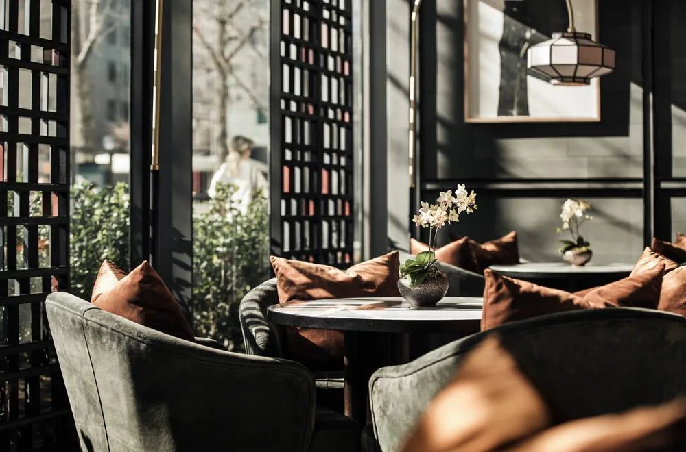 Velvet armchairs and orchids at a tea lounge table beside a dark lattice window