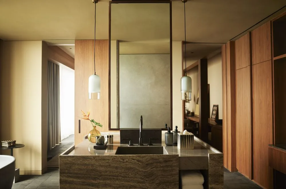 A Rosewood Mandarina suite bathroom with a stone vanity, timber panelling and a hanging mirror