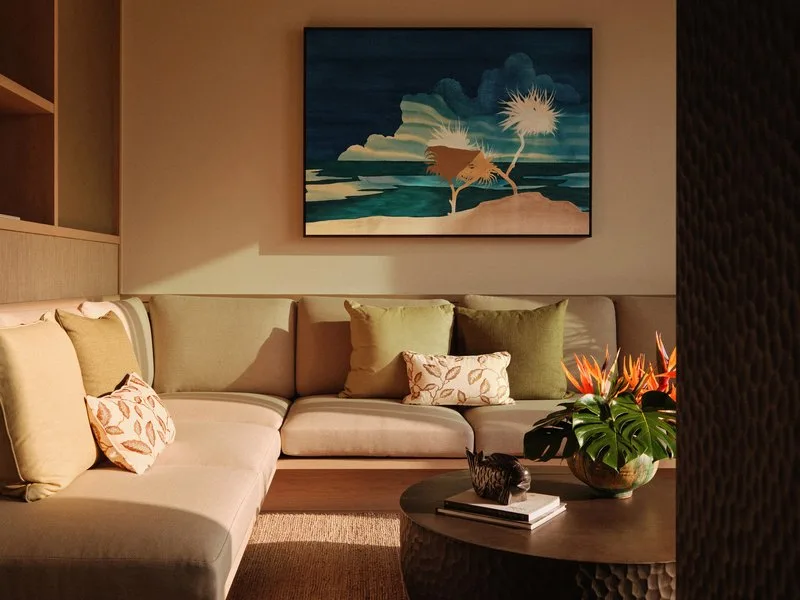 A villa living room at Rosewood Miyakojima with a corner sofa, green cushions, tropical flowers and a painting of an island coastline